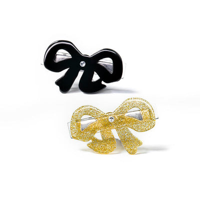 Pair of metal based hair clips adorned with bows. One is black and the other one is gold glitter.