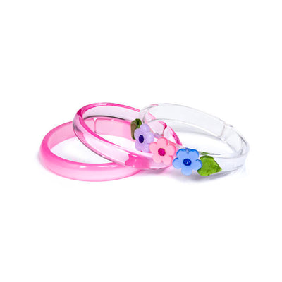 Acrylic set of 3 bracelets. One id clear pink, one is pearlized pink and the last one is clear. The clear bracelet is adorned with a purple flower, a pink flower and a blue flower between green leaves.  