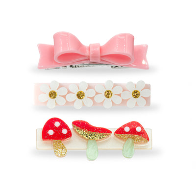 Trio of hair clips. One of them is adorned with a light pink statement bow. The second one has four daisies. And the third one has three red and gold glitter mushrooms. 