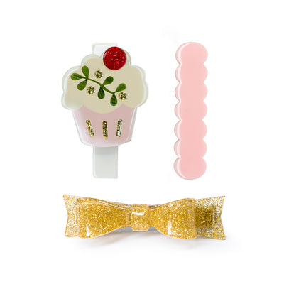 Set of three acrylic hair clips. One is gold glitter bow, one is a light pink cutout and the third one is a cream and pink cupcake adorned with a red glitter ball on top.
